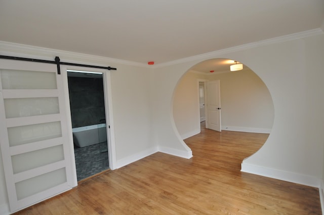 unfurnished room featuring crown molding, a barn door, built in shelves, and light hardwood / wood-style flooring