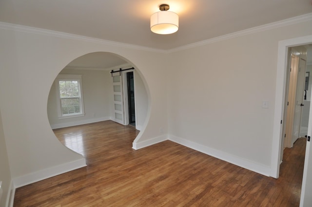 empty room featuring crown molding, a barn door, and hardwood / wood-style floors