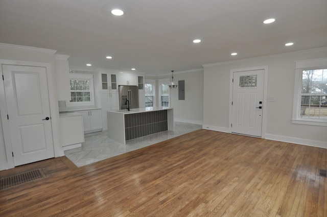 kitchen with a kitchen island, stainless steel fridge, white cabinets, ornamental molding, and electric panel