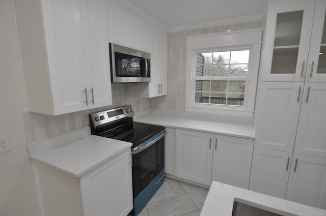 kitchen with stainless steel appliances, light stone countertops, ornamental molding, white cabinets, and decorative backsplash