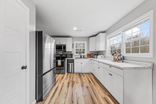 kitchen featuring appliances with stainless steel finishes, sink, white cabinets, and light hardwood / wood-style floors