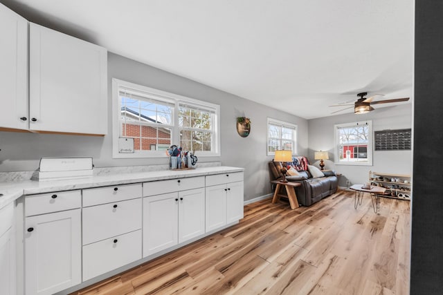 kitchen featuring white cabinetry, light hardwood / wood-style flooring, light stone countertops, and ceiling fan