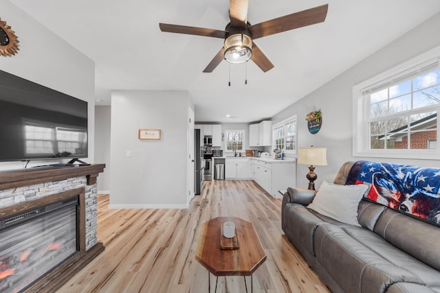 living room featuring sink, a fireplace, ceiling fan, and light wood-type flooring