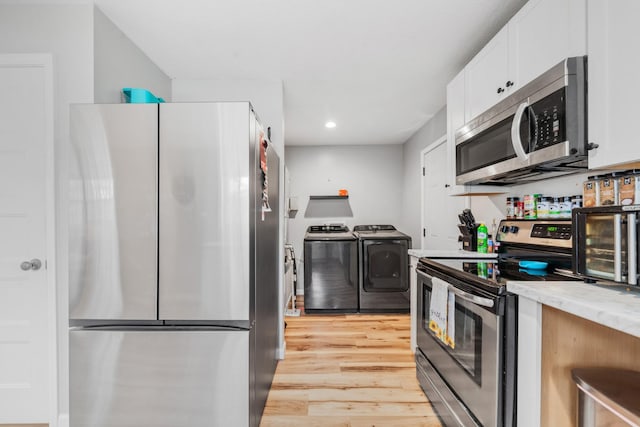 kitchen with white cabinets, light stone counters, stainless steel appliances, washing machine and dryer, and light hardwood / wood-style flooring