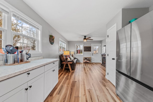 kitchen featuring stainless steel refrigerator, white cabinetry, ceiling fan, light hardwood / wood-style floors, and light stone countertops