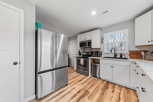 kitchen featuring sink, white cabinetry, light hardwood / wood-style flooring, appliances with stainless steel finishes, and light stone countertops