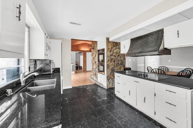 kitchen with sink, custom exhaust hood, dark stone counters, black electric stovetop, and white cabinets