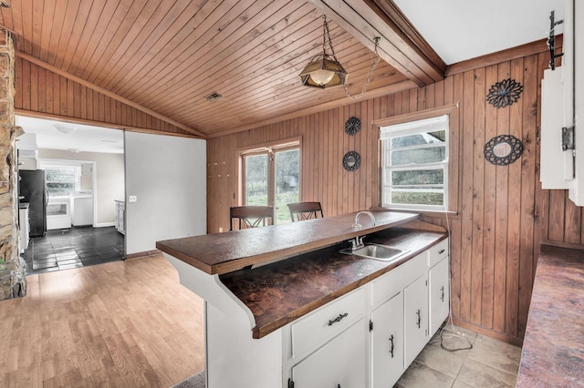 kitchen featuring sink, wooden walls, lofted ceiling with beams, and white cabinets