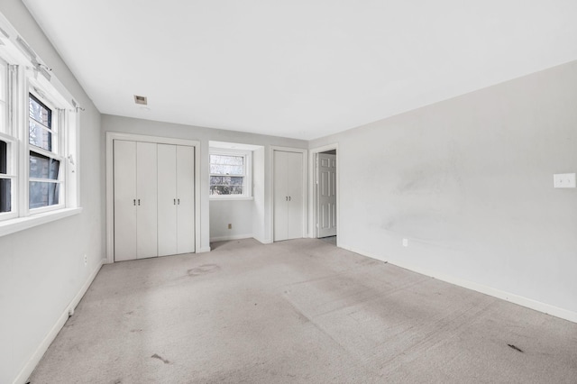 unfurnished bedroom featuring two closets and light colored carpet