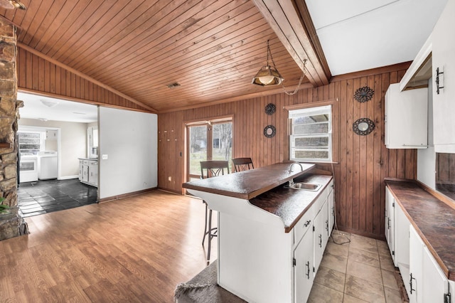 kitchen with washer / dryer, sink, vaulted ceiling with beams, white cabinetry, and wooden walls