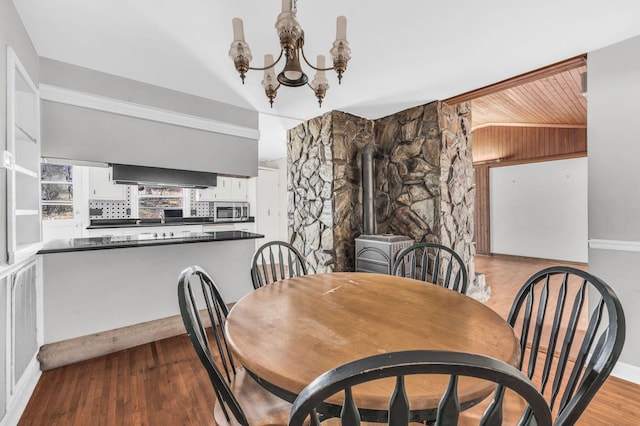 dining room with a notable chandelier, light hardwood / wood-style flooring, vaulted ceiling, and a wood stove