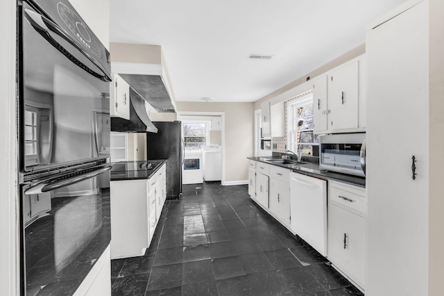 kitchen with white cabinetry, sink, black appliances, washing machine and dryer, and custom range hood