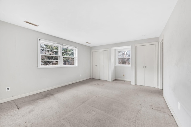 unfurnished bedroom featuring multiple closets and light carpet