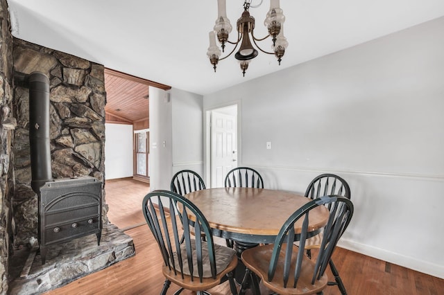 dining room featuring wood-type flooring, a wood stove, and a notable chandelier