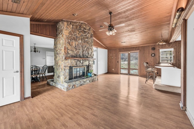 unfurnished living room with vaulted ceiling, a stone fireplace, wooden walls, wood-type flooring, and wood ceiling