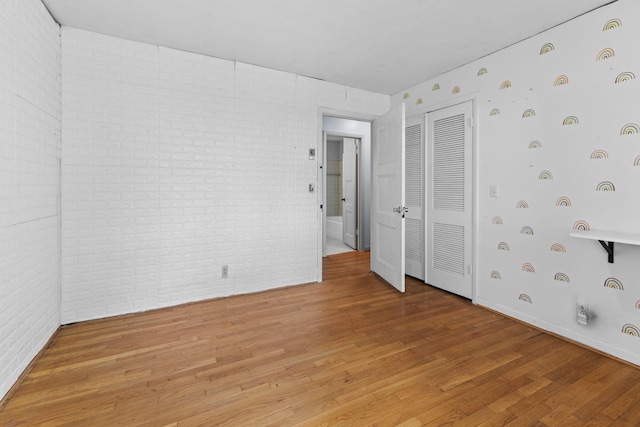 unfurnished bedroom with a closet, light wood-style floors, and brick wall