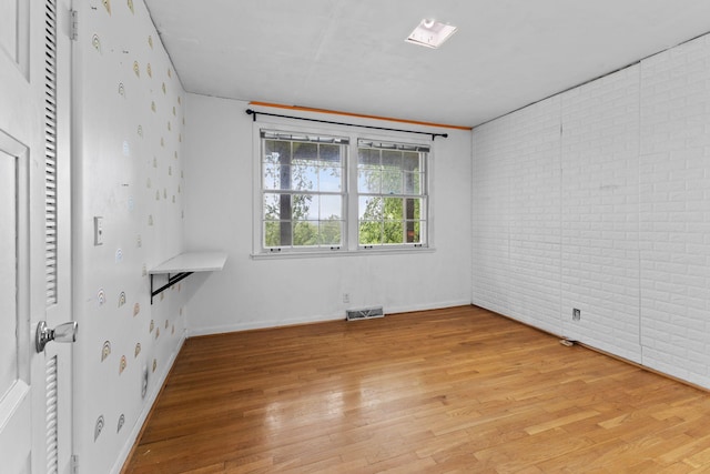 unfurnished room with brick wall, baseboards, visible vents, and light wood-style floors