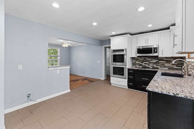 kitchen featuring a sink, stainless steel appliances, decorative backsplash, a ceiling fan, and baseboards