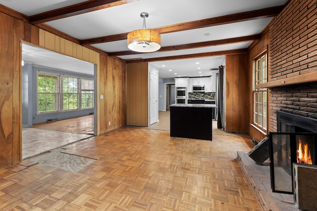 kitchen featuring wooden walls, beamed ceiling, stainless steel appliances, white cabinets, and a large fireplace
