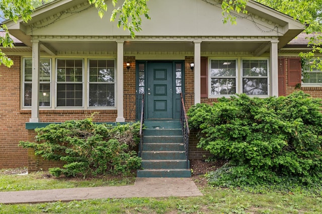 doorway to property featuring covered porch and brick siding