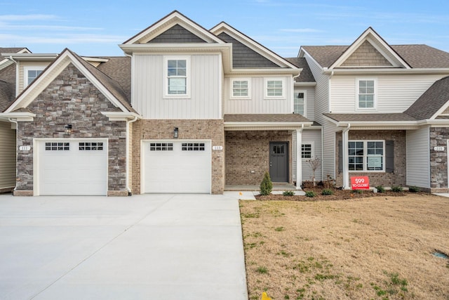 view of front of home featuring brick siding, concrete driveway, stone siding, a front lawn, and board and batten siding