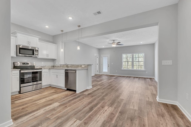 kitchen with open floor plan, stainless steel appliances, hanging light fixtures, and white cabinetry