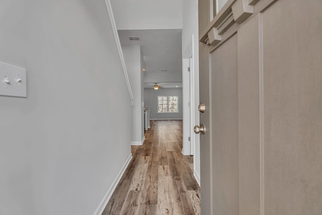 hallway with baseboards, visible vents, and wood finished floors