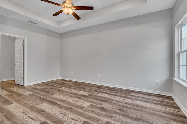 spare room with a tray ceiling, visible vents, baseboards, and wood finished floors