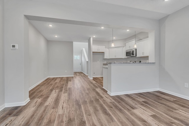 kitchen with baseboards, stainless steel microwave, hanging light fixtures, light wood-type flooring, and white cabinetry