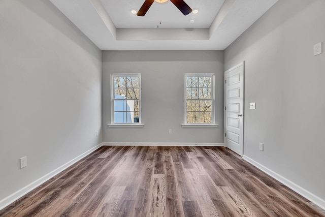 empty room with dark wood-style floors, a ceiling fan, baseboards, and a tray ceiling