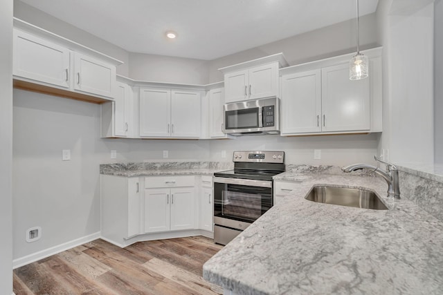 kitchen with stainless steel appliances, a sink, white cabinetry, light wood-style floors, and hanging light fixtures