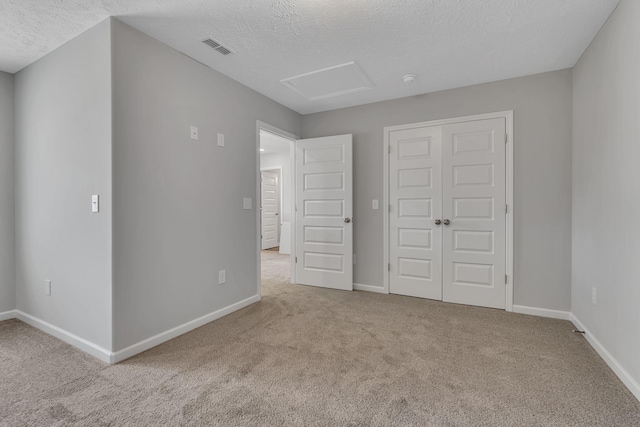 unfurnished bedroom featuring attic access, light colored carpet, visible vents, and baseboards