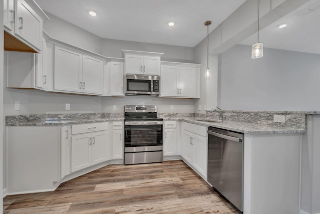 kitchen featuring a sink, white cabinets, appliances with stainless steel finishes, light wood finished floors, and decorative light fixtures