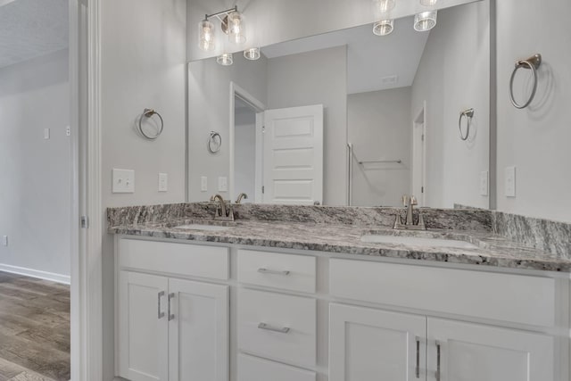 full bath with wood finished floors, a sink, baseboards, and double vanity