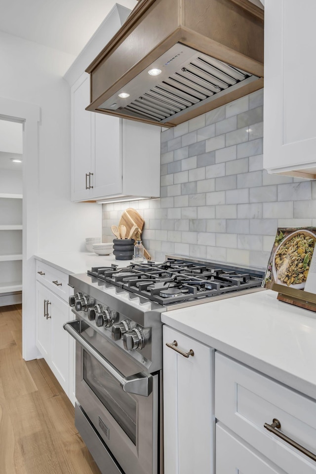 kitchen with stainless steel stove, light hardwood / wood-style flooring, white cabinets, and premium range hood