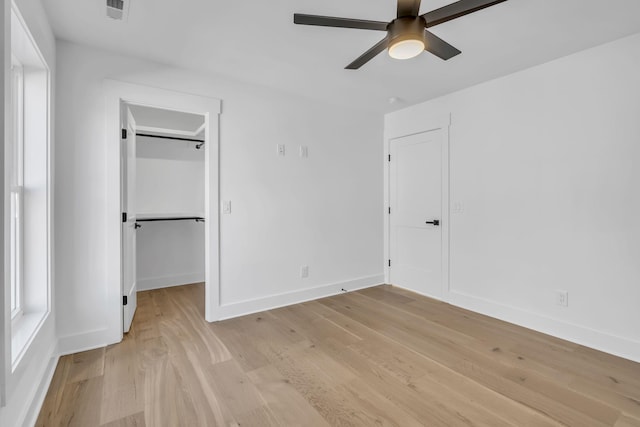 unfurnished bedroom featuring a closet, a spacious closet, ceiling fan, and light hardwood / wood-style flooring