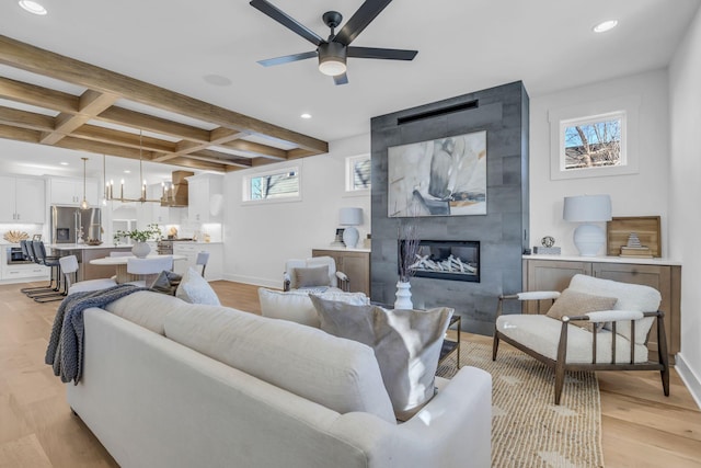 living room with coffered ceiling, a large fireplace, light hardwood / wood-style floors, beamed ceiling, and ceiling fan with notable chandelier