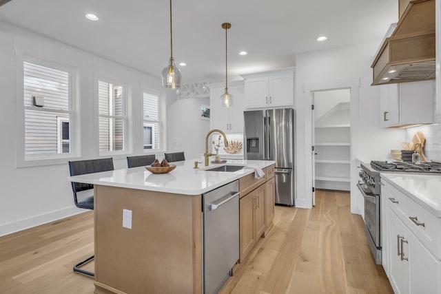 kitchen featuring premium range hood, appliances with stainless steel finishes, pendant lighting, white cabinetry, and an island with sink