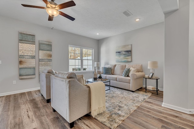 living room featuring hardwood / wood-style flooring, ceiling fan, and a textured ceiling