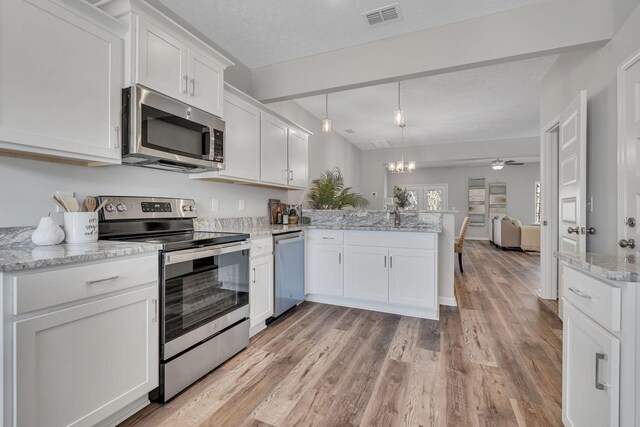 kitchen featuring white cabinetry, kitchen peninsula, hanging light fixtures, stainless steel appliances, and light stone counters