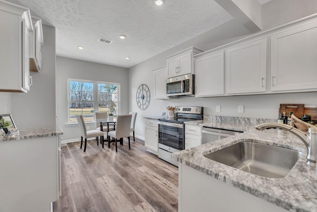 kitchen with white cabinetry, light wood-type flooring, stainless steel appliances, light stone countertops, and sink