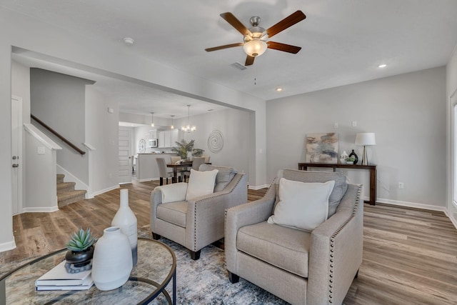 living room featuring ceiling fan with notable chandelier and light hardwood / wood-style floors