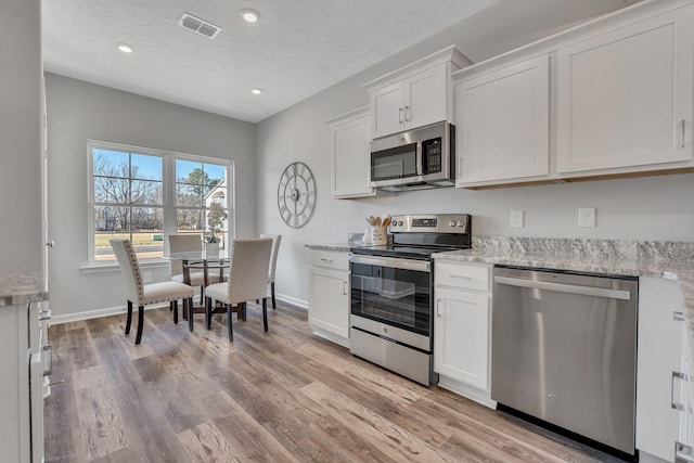 kitchen with white cabinets, light stone countertops, stainless steel appliances, and light hardwood / wood-style floors