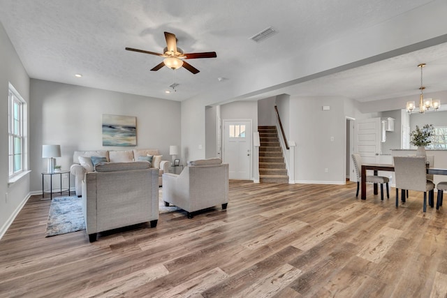 living room with ceiling fan with notable chandelier, wood-type flooring, and a textured ceiling