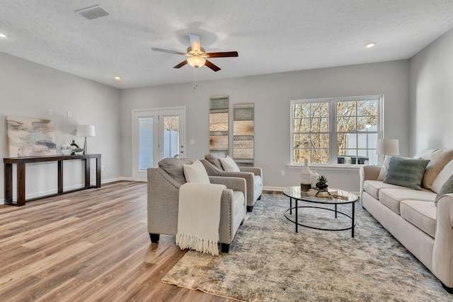 living room featuring light wood-type flooring, a textured ceiling, and ceiling fan