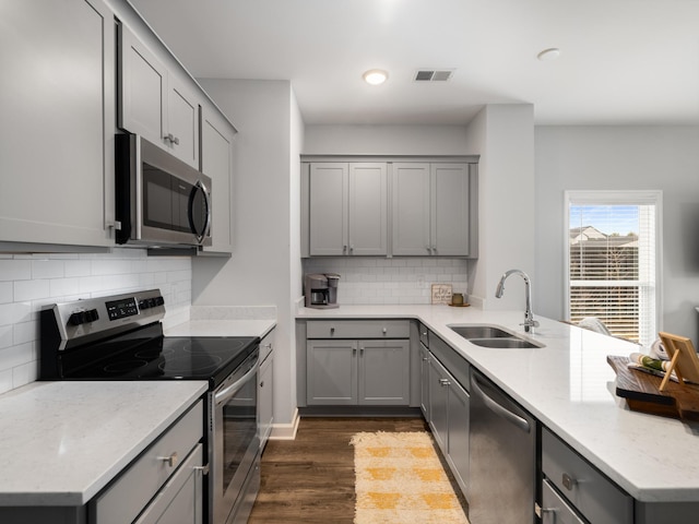 kitchen with gray cabinets, appliances with stainless steel finishes, sink, light stone countertops, and dark wood-type flooring