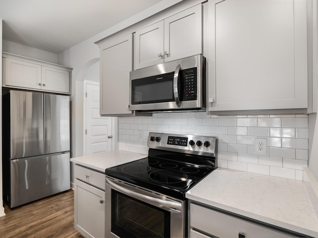 kitchen with tasteful backsplash, appliances with stainless steel finishes, light stone countertops, and wood-type flooring