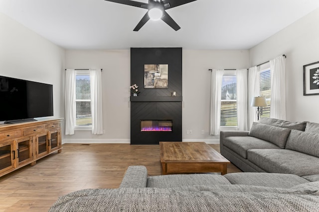 living room featuring a large fireplace, ceiling fan, and light hardwood / wood-style flooring