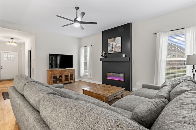 living room with a fireplace, ceiling fan with notable chandelier, and light wood-type flooring