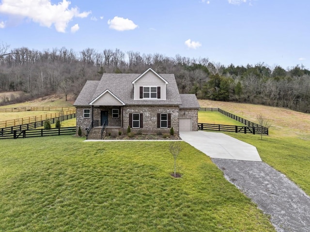 view of front of house with fence, an attached garage, a rural view, a front lawn, and driveway